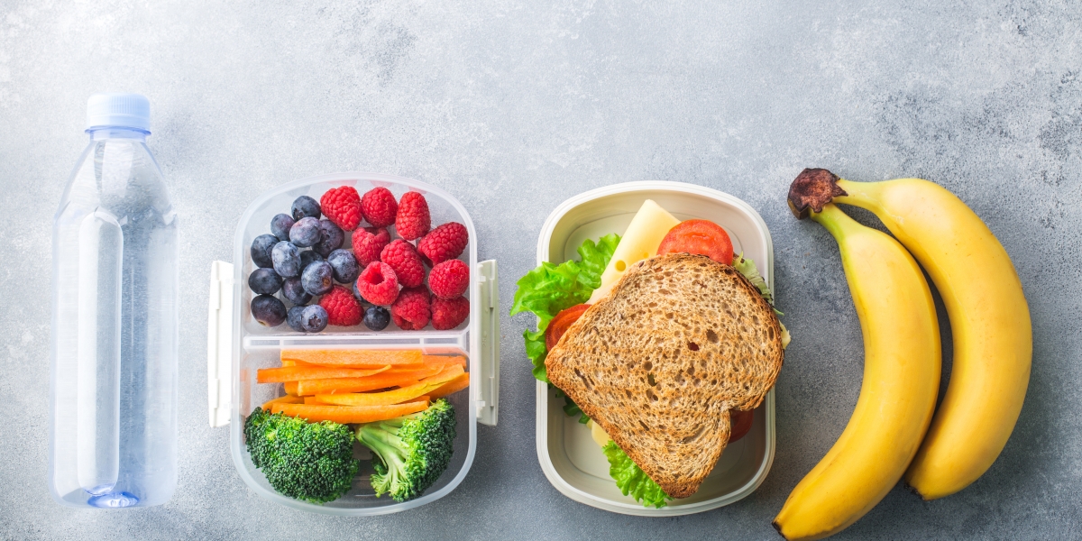School lunch box with sandwich vegetables water almonds and fruits on black chalkboard